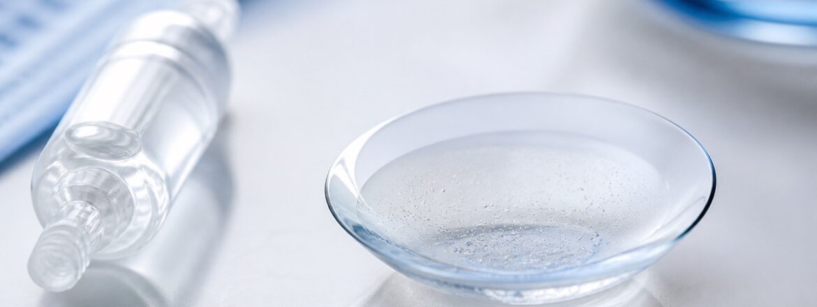 Scleral lens with subtle fluid clouding beside an unbranded preservative-free saline vial
